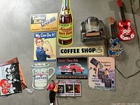 Top view of assorted 1950s themed metal signs, a mini jukebox model, two toy guitars, and Elvis dolls with TV guides scattered on the floor.
