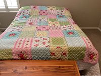 Quilt spread on bed showing patchwork squares in pink, blue, green, yellow with rose floral motifs