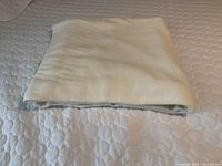 Folded cream-colored Egyptian cotton blanket on a white quilted surface, showing the texture and fabric quality.