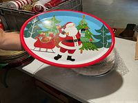 Round holiday charger featuring Santa Claus in front of Christmas trees, red rimmed