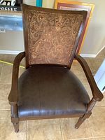 Large brown leather seat with stitching, high paisley upholstered back with wooden frame, armrests, and legs