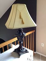 Table lamp with detailed base and cream pleated fabric shade with tassel, unlit condition