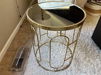 Side angle view of the round mirrored accent table on carpet with visible vent and partial chair.