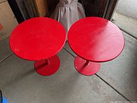 Top view of two identical round red metal side tables, showing condition and size