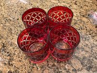 Top-down view of four red cut glass highball drinking glasses with clear etched geometric circular and diamond cut patterns on the sides.