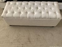 Front view of a white upholstered bench with button tufted top and storage feature.