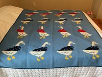 Photo of the blue side of the blanket with rows of white ducks wearing red and navy sweaters and scarves.