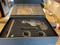 Top view of black foam insert with revolver-shaped whiskey decanter and two shot glasses in the gift box.