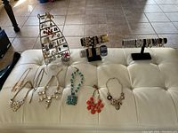 Full view of the lot showing necklaces laid out and earrings on a metal earring holder, along with some bracelets on a black display stand.