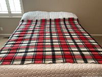 Top view of red, black, and white plaid wool blanket spread on a bed.