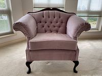 Front view of the rose-coloured upholstered armchair showing the full seat, rolled arms, and wooden cabriole legs.