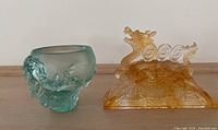 Amber glass dragon figure standing on decorative base with wave and cloud design next to blue-green textured art glass vase.