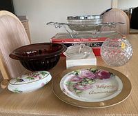 Full view of all items on table including Mikasa ashtray, china trinket container, crystal bowls, decorative floral plate, Arcoroc boxed bowl set with metal stand, glass serving bowl.
