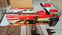 Photo showing Homelite electric chain saw with safety guard and original box, plus bottle of Jager bar and chain oil and part of hedge trimmer.