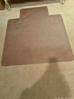 Brown textured chair mat with notched edges laid on carpet.
