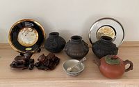 Full lot overview showing 2 Chokin 24k gold decorative plates, 3 black pottery vases/jars, pewter salt dish with spoon, pumpkin-shaped teapot, and 2 Asian-style figurines.
