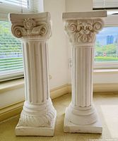 Pair of white plaster columns standing next to a window, showing fluted shafts and ornate capitals