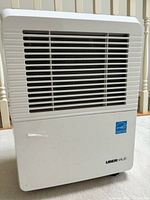 Front view of UberHaus dehumidifier showing white body, vent grill, and logo.