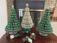 Three electric tabletop Christmas trees displayed on table including two green/red and one clear/white with green accents, all with electric cords and plugs visible. Trees approximately 12 inches tall, topped with clear plastic star.