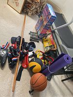 Photo of martial arts and exercise equipment including foot guards, gloves, dumbbells, medicine ball, basketball, wooden staff, and yoga mat
