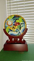 Front view of the round porcelain clock featuring a colorful fish and aquatic design on a wooden stand.