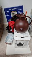 Photo showing various kitchen items including the brown Aril vacuum jug on a box, red Braun coffee grinder, Pyrex bakeware container, blue microwave oven stackers box, and a dark divided basket tray.