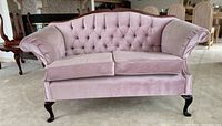 Front view of the rose-coloured upholstered love seat showing button tufted back, seat cushions, and rolled arms on curved wooden legs.