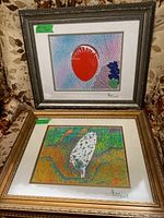 Two framed colorful prints placed one above the other on floral upholstery, showing detailed patterns and signature.