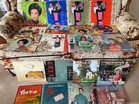 Wide view of approximately 20 Asian vinyl records arranged on a sofa showing colorful album covers with portraits, stylized art, and traditional themes