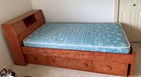 Full view of single wooden bed frame with blue mattress and three storage drawers beneath.