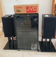 Stereo cabinet with stacked audio components, remote control on top of left speaker, JVC turntable box on top of cabinet, Paradigm speakers on stands.