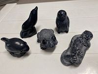 Five black animal sculptures on a white surface including seal, penguin, frog, otter, and whale.