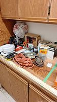 Photo showing various tools and hardware items on a wooden countertop including a hacksaw, crowbar, wrench set, snips, a saber saw, Craftsman circular saw, orange extension cord, and hardware boxes.