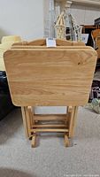 Front view of four wooden TV trays folded and stored upright on a wooden rack.