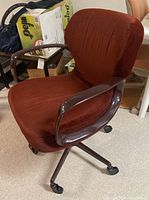 Side-angle view of brown velvet office chair showing cushioned seat, rounded backrest, wooden armrests, and caster wheel base.