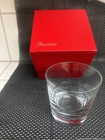 Clear Baccarat French crystal vase in front of its original red Baccarat box with gold logo, placed on dark woven background.