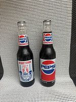 Two unopened Pepsi commemorative long neck glass bottles, one with Desert Storm July 4 1991 Welcome Home label, the other with classic Pepsi label.
