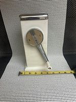 Front view of white vertical rectangular ice crusher with chrome hand crank and labeled circular plate 'ICE-O-MAT'.