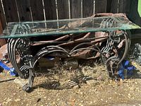 Front view of wrought iron table with beveled glass top placed outdoors on ground, showing full table and ornate scroll iron legs.