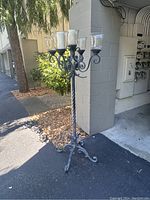 Full view of the tall black wrought iron candelabra with five clear glass candle holders on top, outdoor setting.