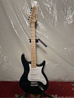 Full front view of black Behringer electric guitar showing body, neck, and headstock with maple fretboard and white pickguard.