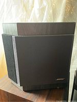 Front angled view of one BOSE 2001 speaker showing wood grain finish and black textured grill with BOSE logo.