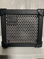 Front view of the Roland Micro Cube amplifier showing the metal mesh speaker grille and Roland logo.