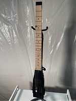 Full front view of matte black headless travel guitar on stand