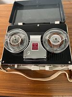 Vintage mini reel-to-reel tape recorder with clear tape reels inside black hinged case, silver metal panel center with model number A441