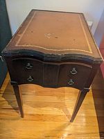 Front view of one of the antique side tables showing leather top with gold embossing and two drawers with metal handles.