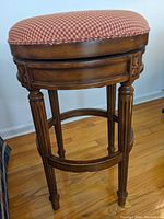 Single wooden bar stool with cushioned gingham seat showing fluted legs and carved detailing beneath the seat.