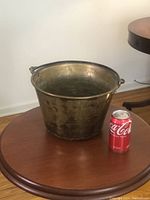 Front view of a hammered brass bucket placed on a wooden table with a Coca-Cola can for size reference.