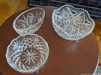 Three different crystal glass bowls on a wooden surface, showing detailed cut glass patterns and different sizes