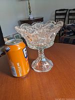 Crystal glass goblet next to an orange soda can for size comparison on wooden table.